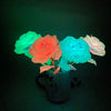 A bouquet of glowing foil roses in shades of green, orange, blue, and white, illuminated against a dark background.