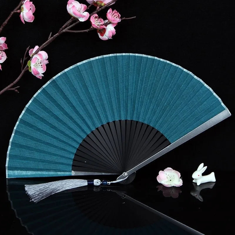 A teal titanium alloy folding hand fan with pink blossoms is displayed against a black background.