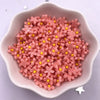 A pile of pink 3D resin flower gems with yellow centers in a light colored dish.
