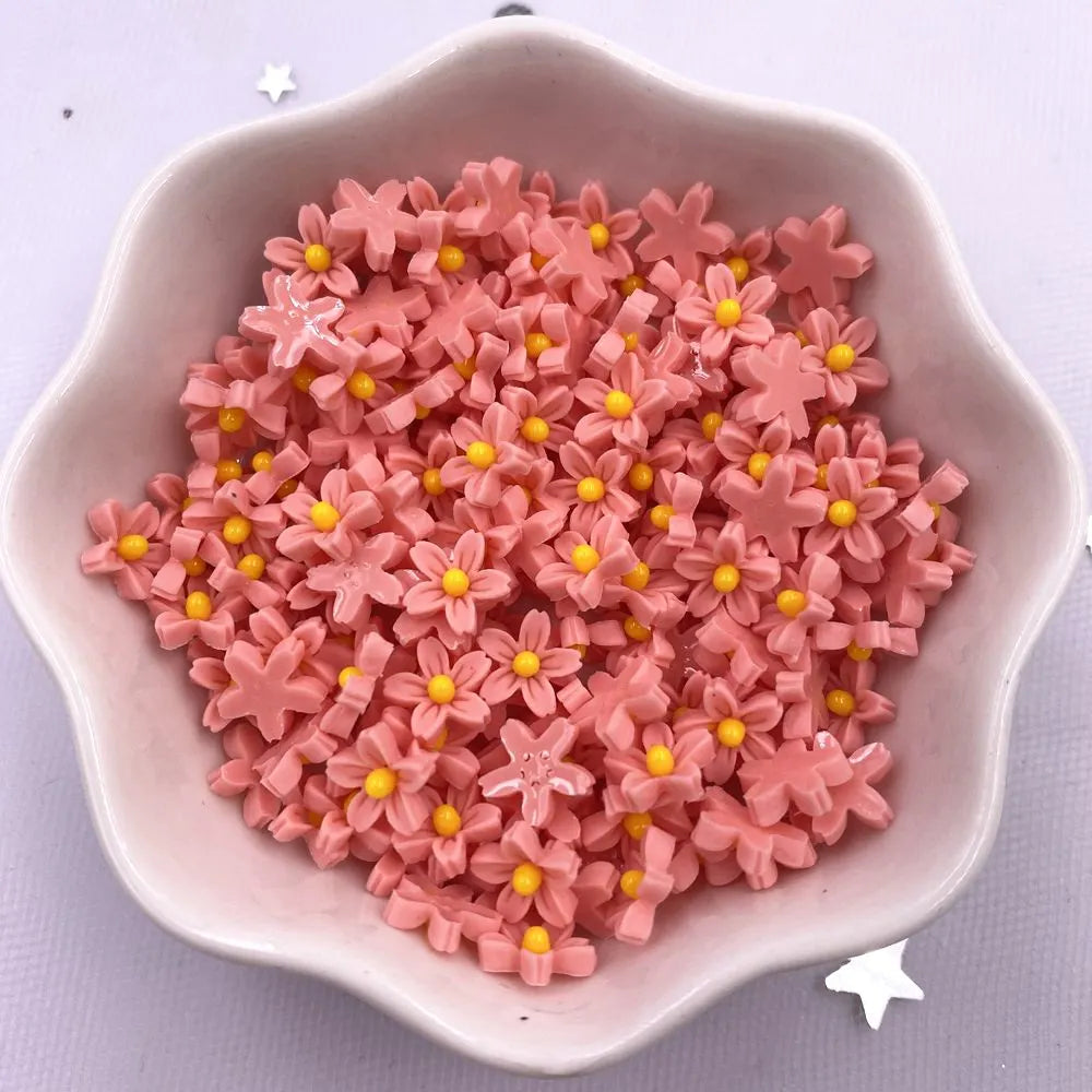A pile of pink 3D resin flower gems with yellow centers in a light colored dish.