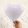 A silver heart-shaped foil balloon is being held, displayed on a white textured surface.