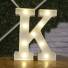 A large illuminated letter K made of warm white LED alphabet light resting on a wooden surface.