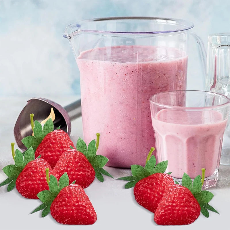 A glass pitcher filled with pink strawberry smoothie next to fresh red strawberries and green leaves.