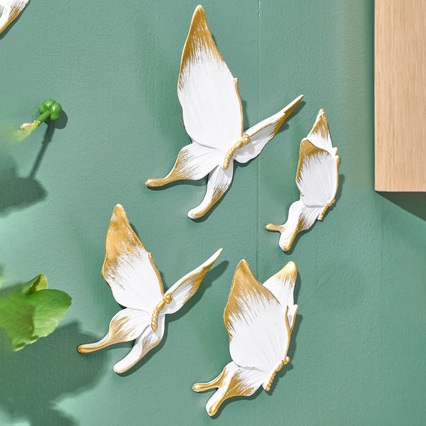 A set of handcrafted resin butterflies in white and gold are displayed against a muted green wall.