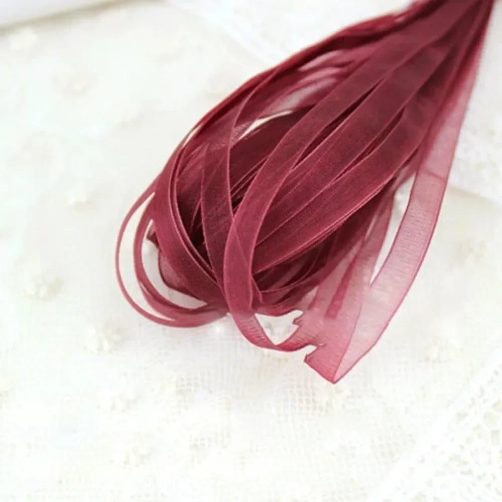 A bundle of deep burgundy decorative fishtail yarn ribbon laid on a white textured cloth.