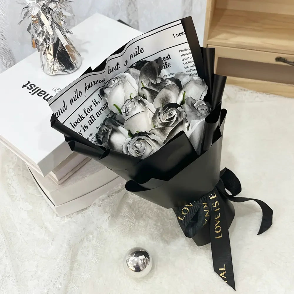 A bouquet of artificial roses wrapped in black paper resting on a stack of white books.