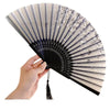A hand holds an elegant floral bird print bamboo folding fan, showing its pleated design and light beige color.