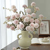 A bouquet of pink silk chrysanthemum artificial flowers in a light ceramic vase on a wooden table.