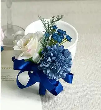 A bouquet of dusty blue silk roses and blue flowers tied with a deep blue ribbon in a white cup.