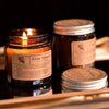 A hand-poured soy aromatherapy candle in a glass jar with a gold lid sits on a wooden surface.