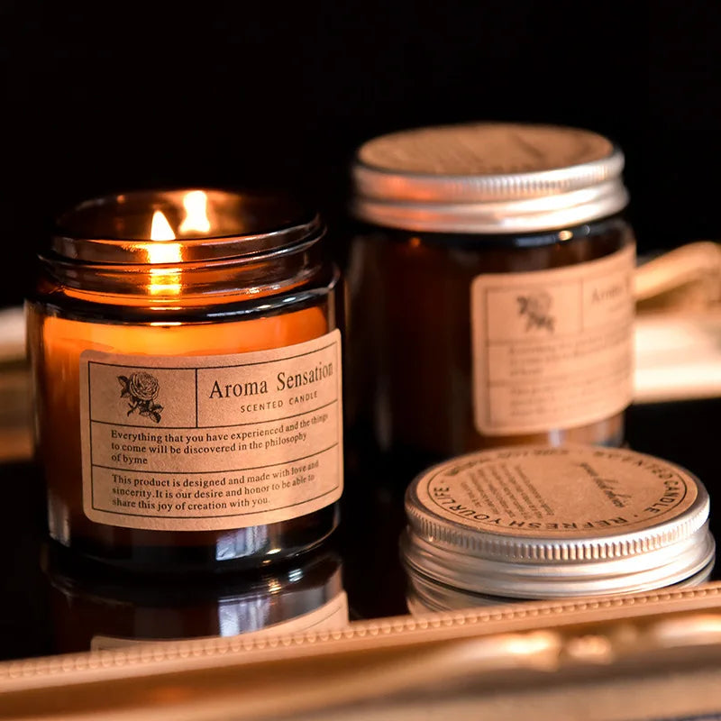 A hand-poured soy aromatherapy candle in a glass jar with a gold lid sits on a wooden surface.
