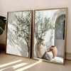 A framed painting featuring an olive tree branch in a terracotta vase against a white background.