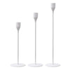 A set of three elegant metal candle holders with tall, slender white stems.
