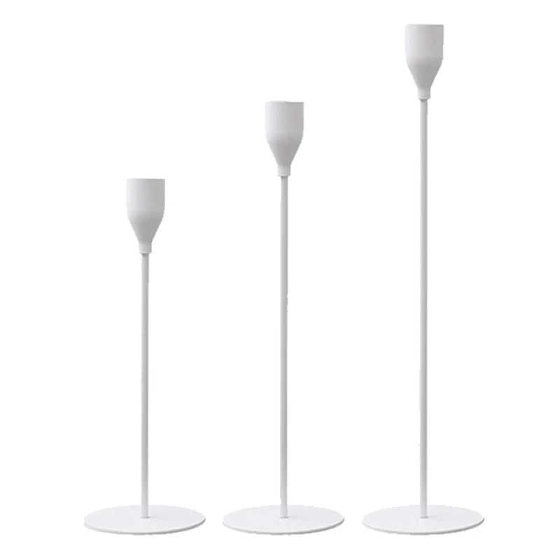 A set of three elegant metal candle holders with tall, slender white stems.