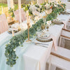 A white table setting decorated with a green vine garland and white flowers for an event.