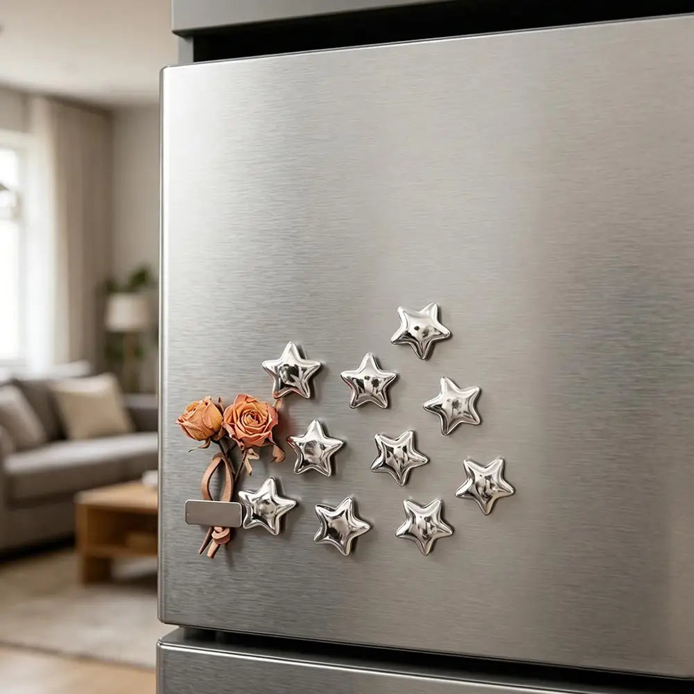 A close-up of a stainless steel refrigerator featuring ten silver star-shaped magnets with rose gold accents.