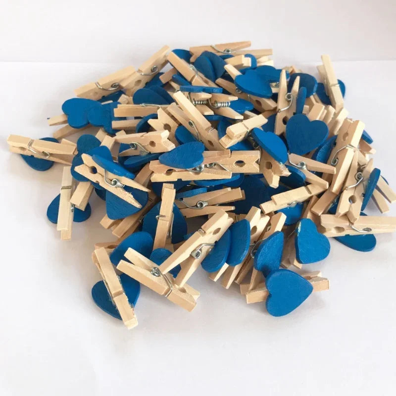A pile of small wooden photo clips shaped like hearts in various shades of blue.