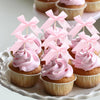 A display of pink frosted cupcakes with pink bow toppers on a white platter.