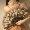 A close-up of an elegant lace rose folding fan with intricate floral patterns and dark accents.