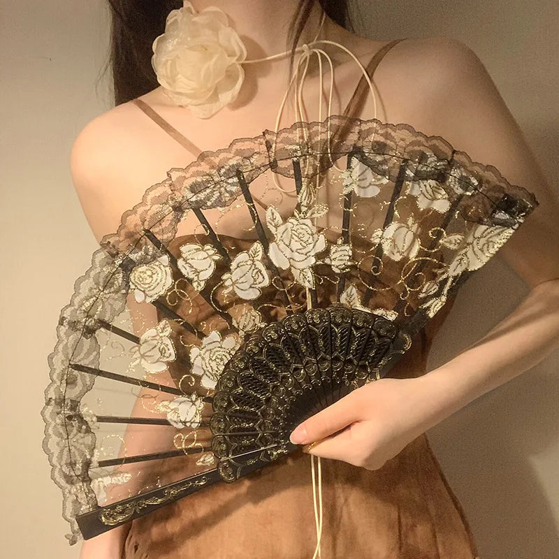A close-up of an elegant lace rose folding fan with intricate floral patterns and dark accents.