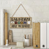 A vintage wooden farmhouse hanging sign with the text Laundry Room Help Wanted mounted on a white brick wall.