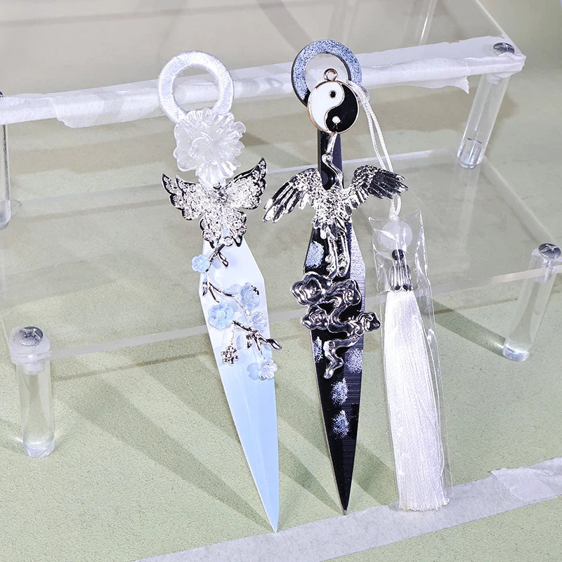 A dark decorative kunai utility knife with a silver loop and intricate black and white detailing is displayed on a clear acry