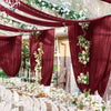 Deep burgundy sheer chiffon curtains draped with white floral garlands for a wedding event backdrop.