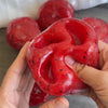 A hand holds a bright red, textured cheese squishy stress relief toy filled with Vaseline.
