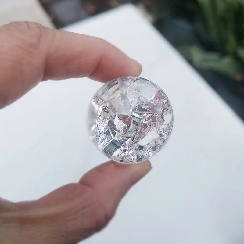 A hand holds a clear, round crystal ice crack ball water fountain decor.