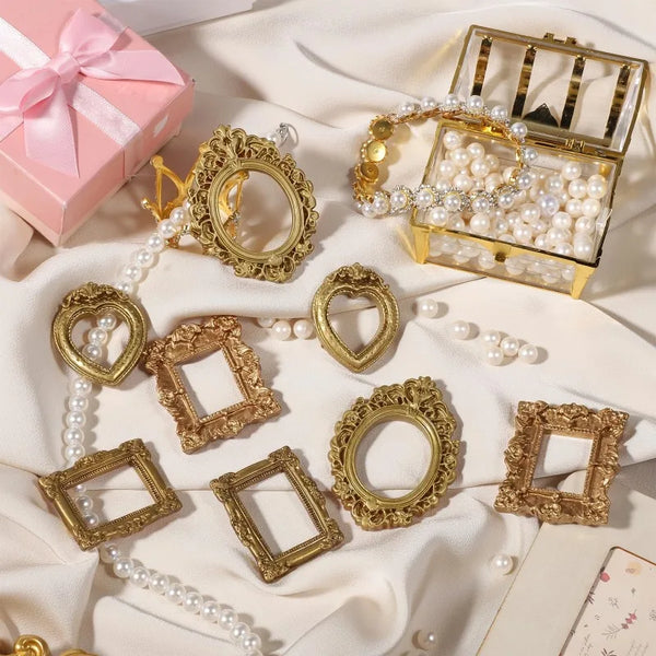 A collection of vintage baroque resin picture frames and a gold-toned jewelry box displayed on white fabric.