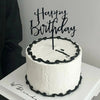A white cake with black piping and a black acrylic topper that reads Happy Birthday