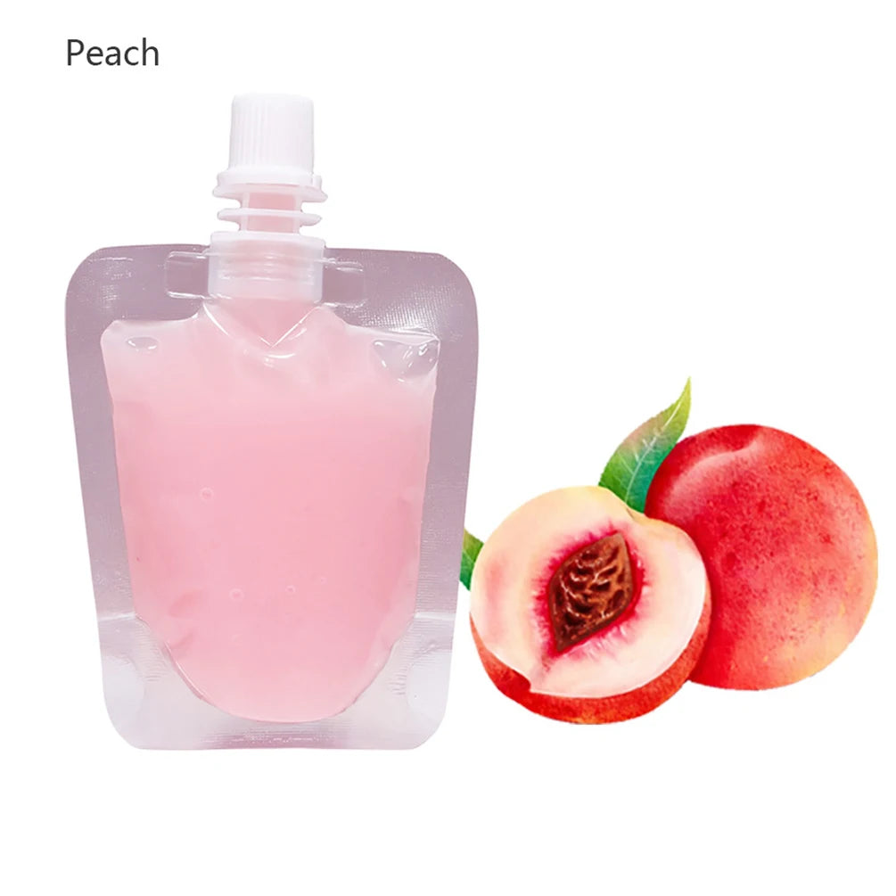 A clear plastic bottle of peach flavored lip oil gloss next to a fresh peach fruit.