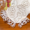 A set of white cookie cutters and fondant stamps shaped like a pumpkin, skull, hand, and other Halloween figures on a wooden 