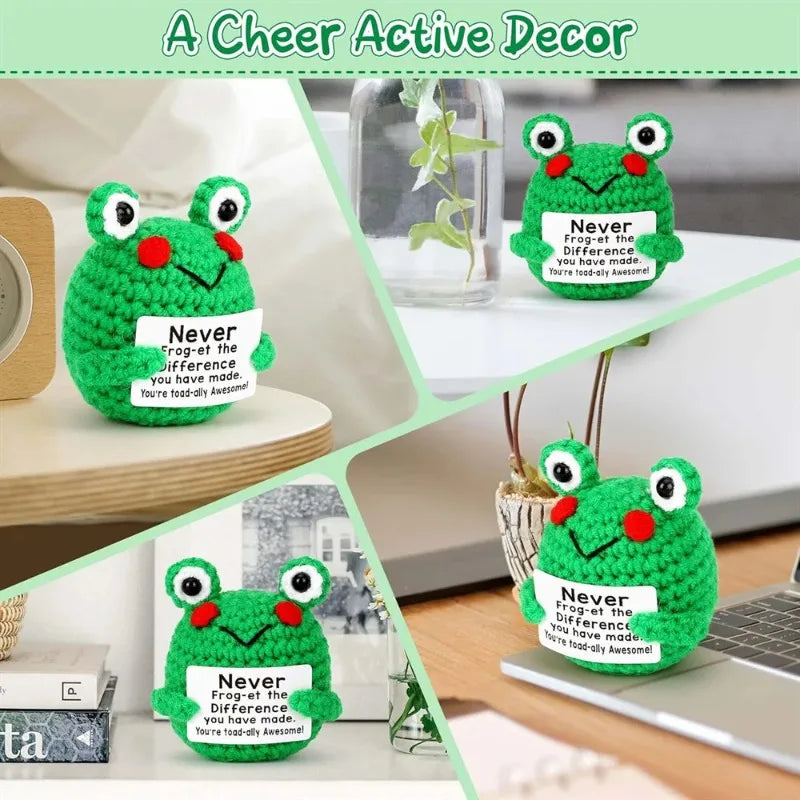 A green crochet frog ornament with a happy expression displayed on a white surface.