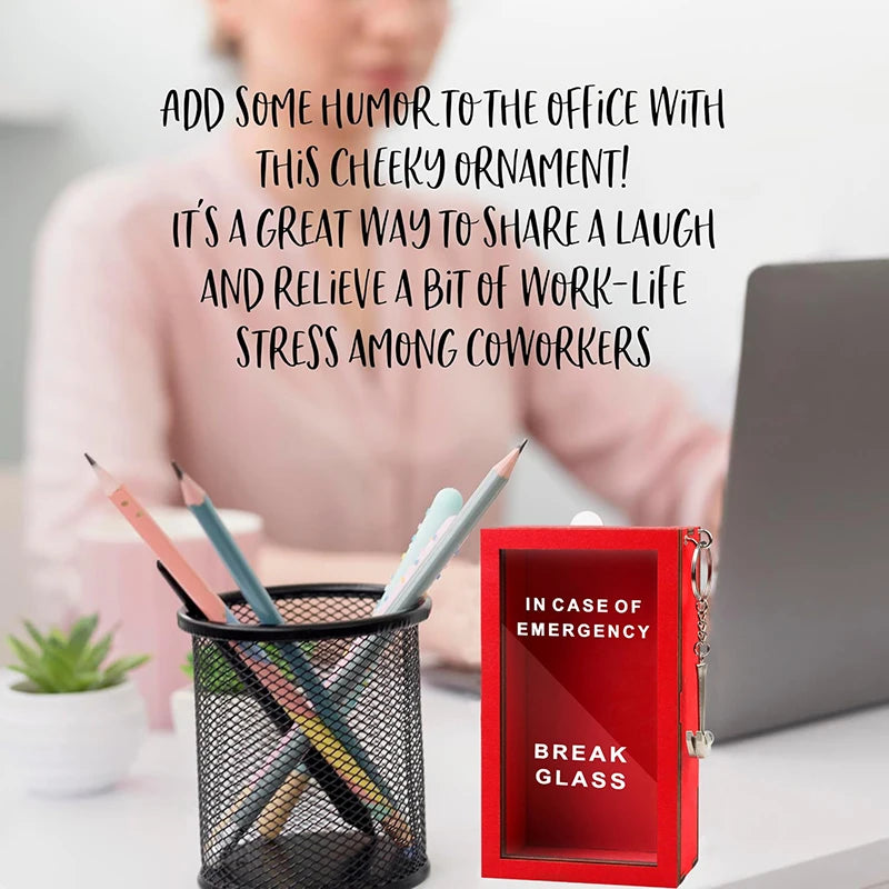 Una caja de regalo roja etiquetada 'Break Glass' junto a una planta en maceta y una laptop.
