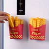 A hand is holding a red container of yellow French fry shaped sealing clips on a white surface.