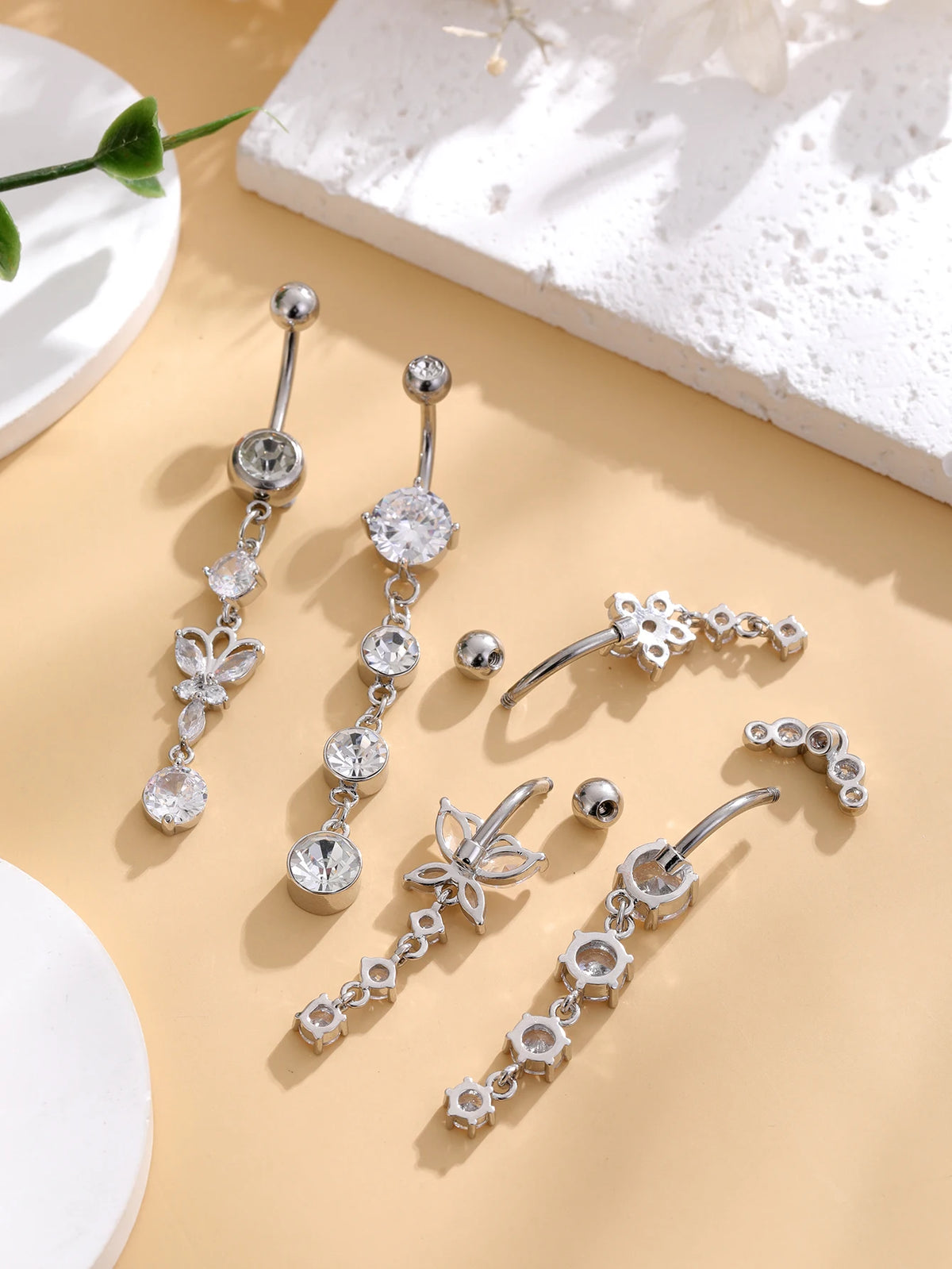 A set of five gold tone butterfly and flower belly rings displayed on a light beige background.