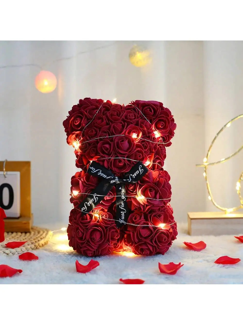 Roter künstlicher Rosen-Teddybär, beleuchtet mit warmen Lichtern, liegt auf einer weißen Oberfläche.