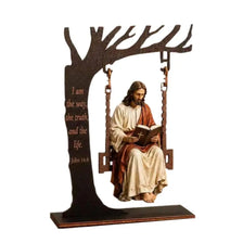 A wooden ornament depicting Jesus reading a Bible, mounted on a tree branch structure.