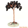 A natural crystal money tree decor featuring black obsidian leaves on a copper wire stem and light green base.