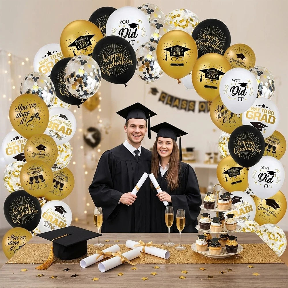 A collection of black and gold graduation balloons with cap and star designs arranged on a wooden surface.