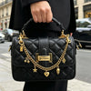 A black quilted handbag with gold chain detailing is held by a person in a dark suit.