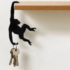 Black silhouette of a monkey figure with an outstretched hand and a banana design attached to a hook