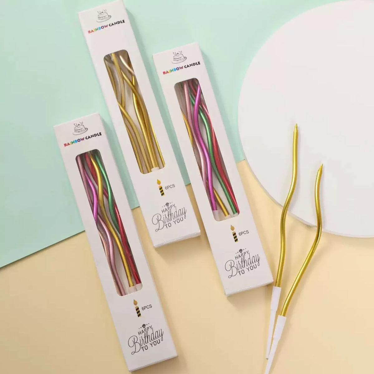 A set of six metallic twisted coil birthday candles in various colors are displayed on a light green and beige background.
