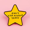 A yellow star enamel pin with black outline featuring the text didn't bite anyone today.