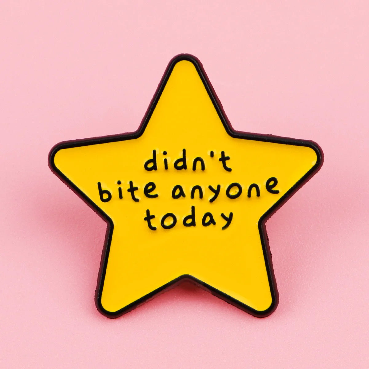 A yellow star enamel pin with black outline featuring the text didn't bite anyone today.