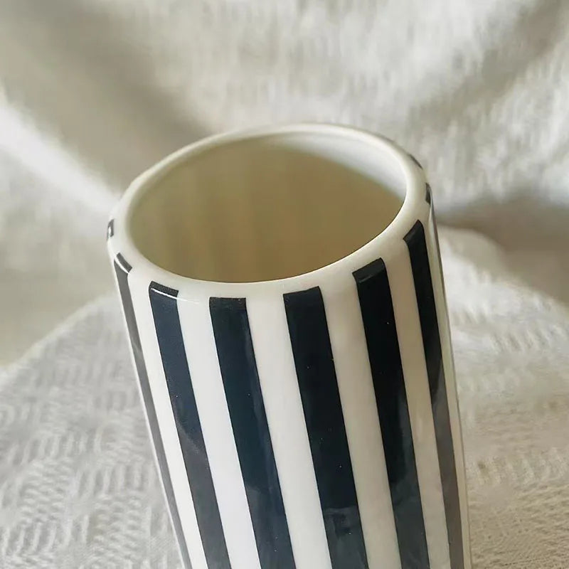 A ceramic tabletop vase with vertical black and white stripes is shown against a white fabric background.