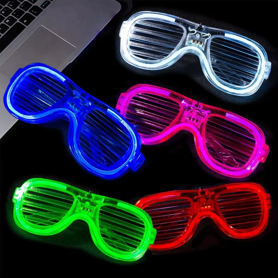 A collection of four LED light-up glow glasses in blue, pink, green, and red lying on a dark surface.