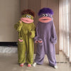 A pair of fuzzy, green and purple monster coral fleece hooded sleepsuits for women.