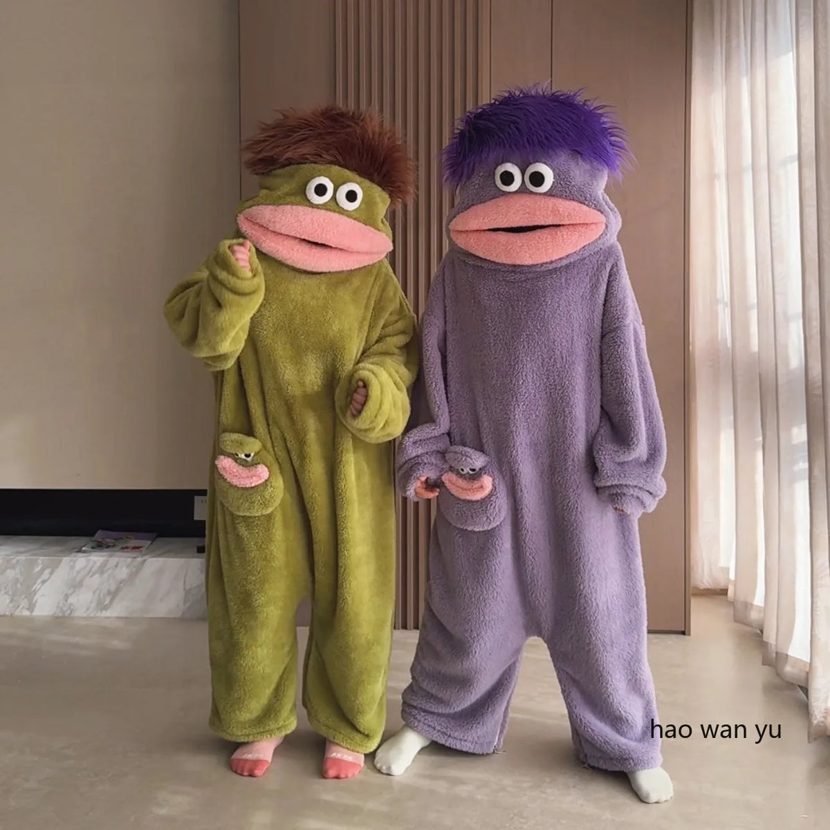 A pair of fuzzy, green and purple monster coral fleece hooded sleepsuits for women.